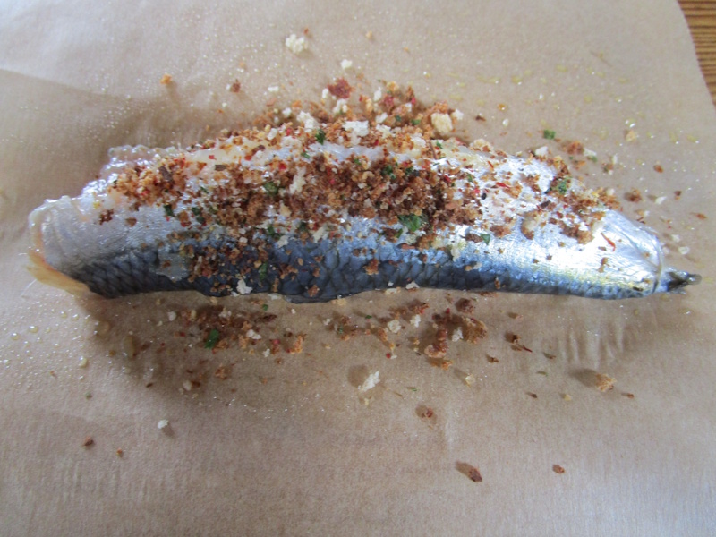 Las sardinas se sazonan con especias, perjejil y migas de pan en un papel untado de aceite, que se pliega para convertirse en una caja.